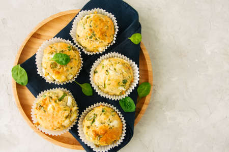 Savory muffins with feta cheese and spinach on a wooden plate on a white stone backdrop. の写真素材