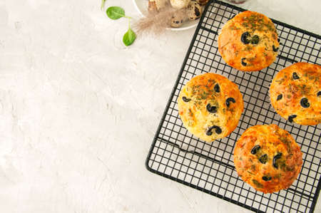 Savory muffins with olives and herbs on a wire rack on a white stone backdrop. Rustic style.の写真素材