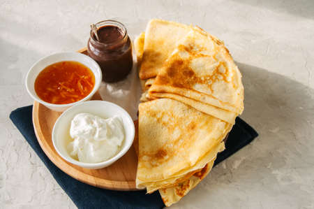 Delicious crepes (blinis) with assorted sauces on a wooden plate on a white stone background.の写真素材