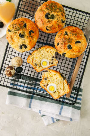 Savory muffins with olives and herbs on a wire rack on a white stone backdrop. Top view.の写真素材