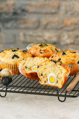 Savory muffins with olives and herbs on a wire rack on a white stone backdrop. 