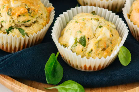 Savory muffins with feta cheese and spinach on a wooden plate on a wire rack.White stone backdrop. の写真素材