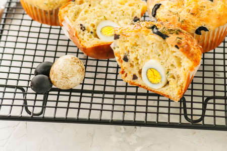 Savory muffins with olives and herbs on a wire rack on a white stone backdrop. の写真素材
