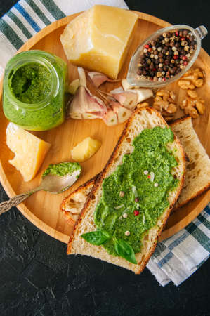 Bruschetta with basil walnut pesto sauce on a wooden plate. Black stone backdrop.の写真素材
