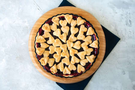 Cherry pie with heart shape decorations from flaky dough on a white backdropの写真素材