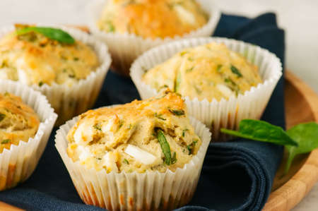 Savory muffins with feta cheese and spinach on a wooden plate on a wire rack.White stone backdrop. の写真素材