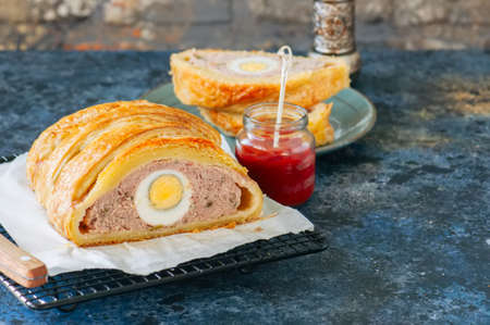 Turkey meatloaf with egg filling in a puff pastry served on a wire rack. Blue stone backdrop.の写真素材