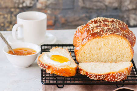 Homemade sesame seeds challah bread on a wire rack, orange jam and a cup of red tea on a white background.の写真素材