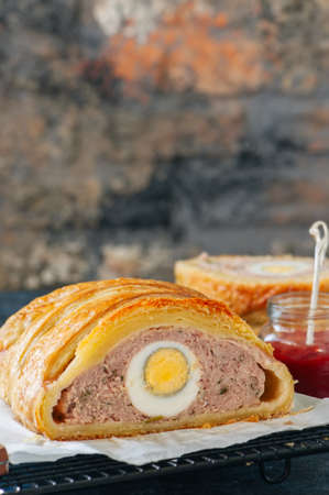 Turkey meatloaf with egg filling in a puff pastry served on a wire rack. Blue stone backdrop.の写真素材