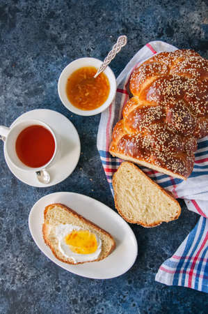 Homemade sesame seeds challah bread, slice of challah with jam  served on a plate and a cup of tea  on a blue background. Overhead view.の写真素材