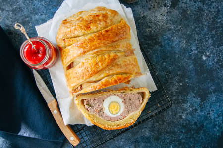 Turkey meatloaf with egg filling in a puff pastry served on a wire rack. Blue stone backdrop.