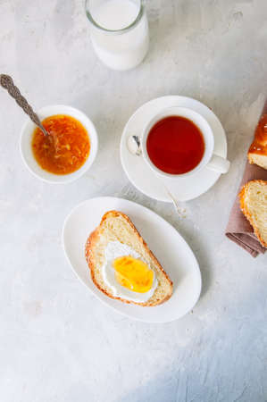 Slice of homemade sesame seeds challah bread with jam, glass of milk and a cup of tea on a white background. Breakfast concept.の写真素材