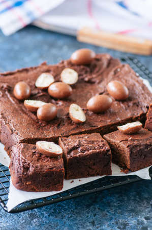 Dark chocolate brownie square on a wire rack decorated with creamy chocolate eggs. Blue stone background.の写真素材
