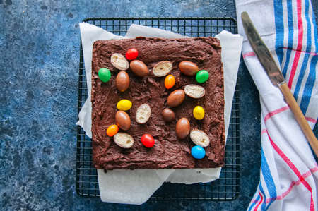 Dark chocolate brownie square on a wire rack decorated with creamy chocolate eggs. Blue stone background.の写真素材