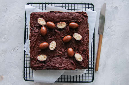 Dark chocolate brownie square on a wire rack decorated with creamy chocolate eggs. Blue stone background.の写真素材