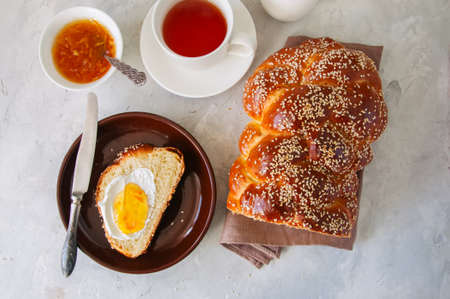 Homemade sesame seeds challah bread, slice of challah with jam  served on a plate and a cup of tea  on a white background.の写真素材