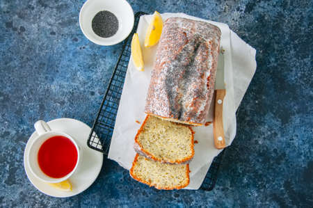 Homemade lemon poppy seed pound cake with glaze on a wire rack, a cup of red tea on a blue stone background.の写真素材