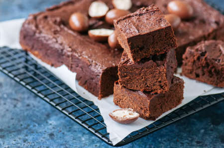 Dark chocolate brownie square on a wire rack decorated with creamy chocolate eggs. Blue stone background.の写真素材