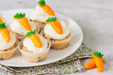 Vanilla cupcakes with chocolate chips and cream cheese frosting decorated with carrot marmalade in a plate on a white stone background.の写真素材