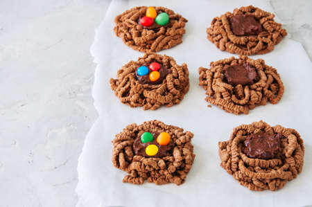 Chocolate bird's nest cookies with ganache and decorated with colorful candies on a white background. Top view and copy space.の写真素材