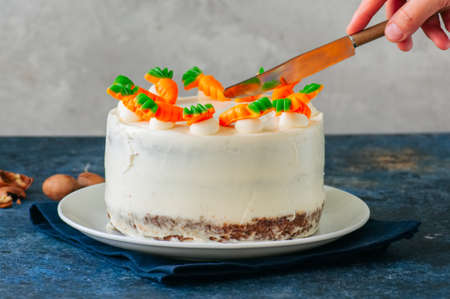 Woman cutting carrot cake with cream cheese frosting decorated with carrot marmalade serving on a...