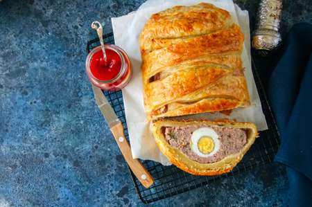 Turkey meatloaf with egg filling in a puff pastry served on a wire rack. Blue stone backdrop.の写真素材