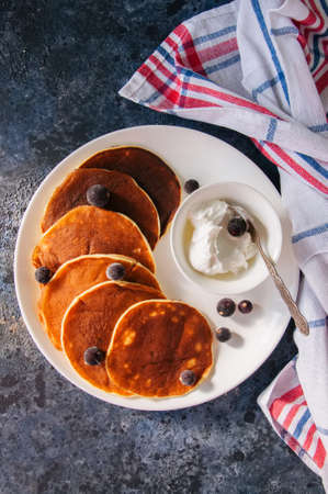 Cottage cheese pancakes with sour cream and berries on a white plate on a blue stone background.の写真素材