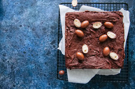 Dark chocolate brownie squares on a wire rack decorated with creamy chocolate eggs. Blue stone...