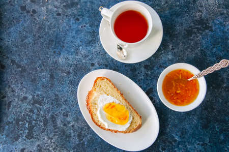 Slice of homemade challah bread with jam and a cup of tea on a blue stone background. Breakfast concept. Top view and copy space.の写真素材