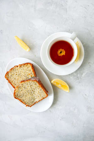 Slices of homemade lemon poppy seed cake served on a white plate, a cup of tea on a white stone background. Top view and copy space.の写真素材