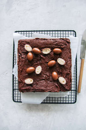 Dark chocolate brownie squares on a wire rack decorated with creamy chocolate eggs. Blue stone...