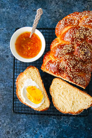 Homemade sesame seed traditional Challah bread, tea, orange jam on a blue stone background. Top...