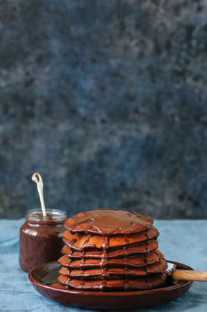 Chocolate pancakes wiyh syrup in a plate on a blue background. Copy space.