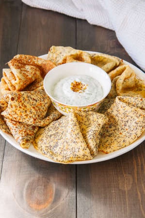 Delicious poppy seed crepes (blinis) and sour cream sauce with dill served on a white plate on a...