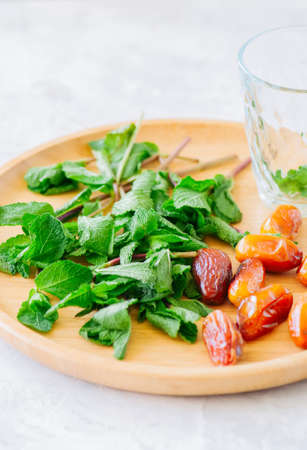 Ingredients for moroccan tea. Mint leaves dates on a wooden plate. White background. の写真素材