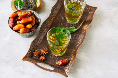 Traditional moroccan mint tea with dates on a vintage tray. White stone background.