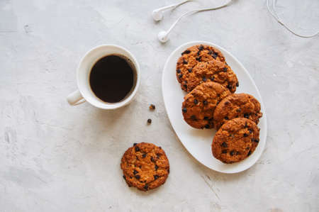 American chocolate chip cookies  in a white plate cup of coffee and headset  on a white stone background. Top view and copy space.の写真素材