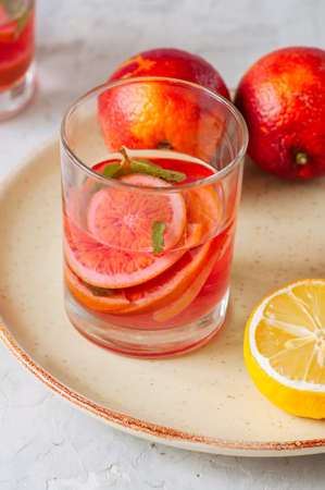 Refreshing blood orange and lemon water or infused water in a glass on a white stone backgroundの写真素材