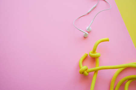 Skipping rope  and headphones on a pink and yellow background. Top view and copy space. Sport, hobby...