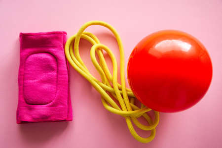 Red gymnastic ball, kneepads and skipping rope on a pink background. Sport, hobby and lifestyle concept. Top view .の写真素材