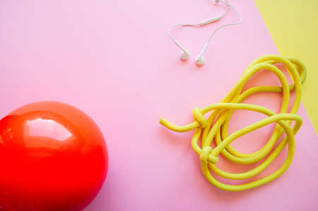 Red gymnastic ball, headphones and skipping rope on a pink and yellow background. Sport, hobby and lifestyle concept. Top view and copy space.の写真素材