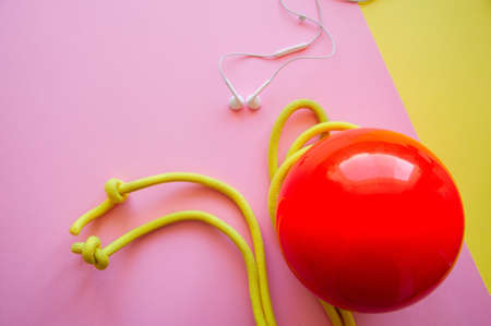 Red gymnastic ball, headphones and skipping rope on a pink and yellow background. Sport, hobby and lifestyle concept. Top view and copy space.の写真素材