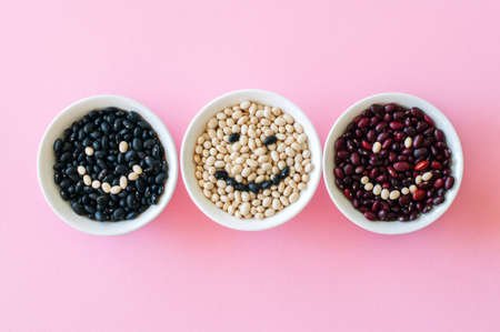 Tree types of dried beans in a white bowls on a pink background. Smile inscription. Top view. Healthy eating concept.の写真素材
