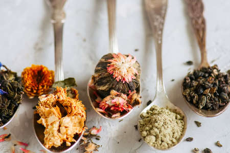 Assortment of dry green herbal and flower tea in a spoons on a white stone background.の写真素材