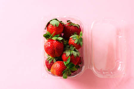 Plastic container with fresh ripe strawberries on a light pink background. Top view and copy space. Organic food concept.の写真素材