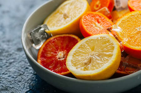 Mix of fresh ripe citrus fruits as blood oranges, mandarines, lemons  with ice cubes in a bowl on a blue stone background.の写真素材