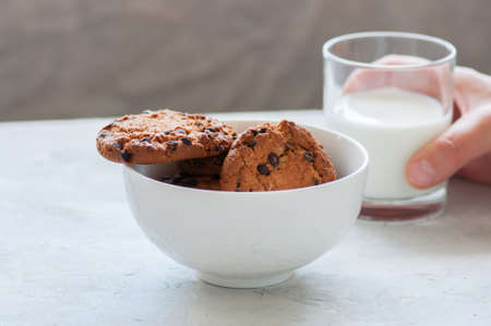 Homemade chocolate chip cookies in a bowl and glass of fresh milk on a white stone background.の写真素材