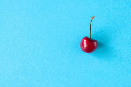 One fresh ripe red cherry on a light blue background. Top view and copy space. Organic food concept.の写真素材