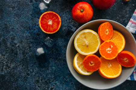 Mix of fresh ripe citrus fruits as blood oranges, mandarines, lemons  with ice cubes in a bowl on a blue stone background.の写真素材