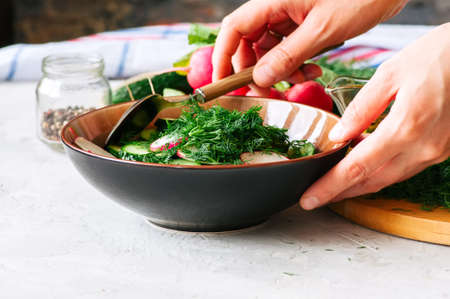 Healthy salad from fresh vegetables in making. Woman's hands mixing salad in a bowl. Cooking step by step concept.の写真素材